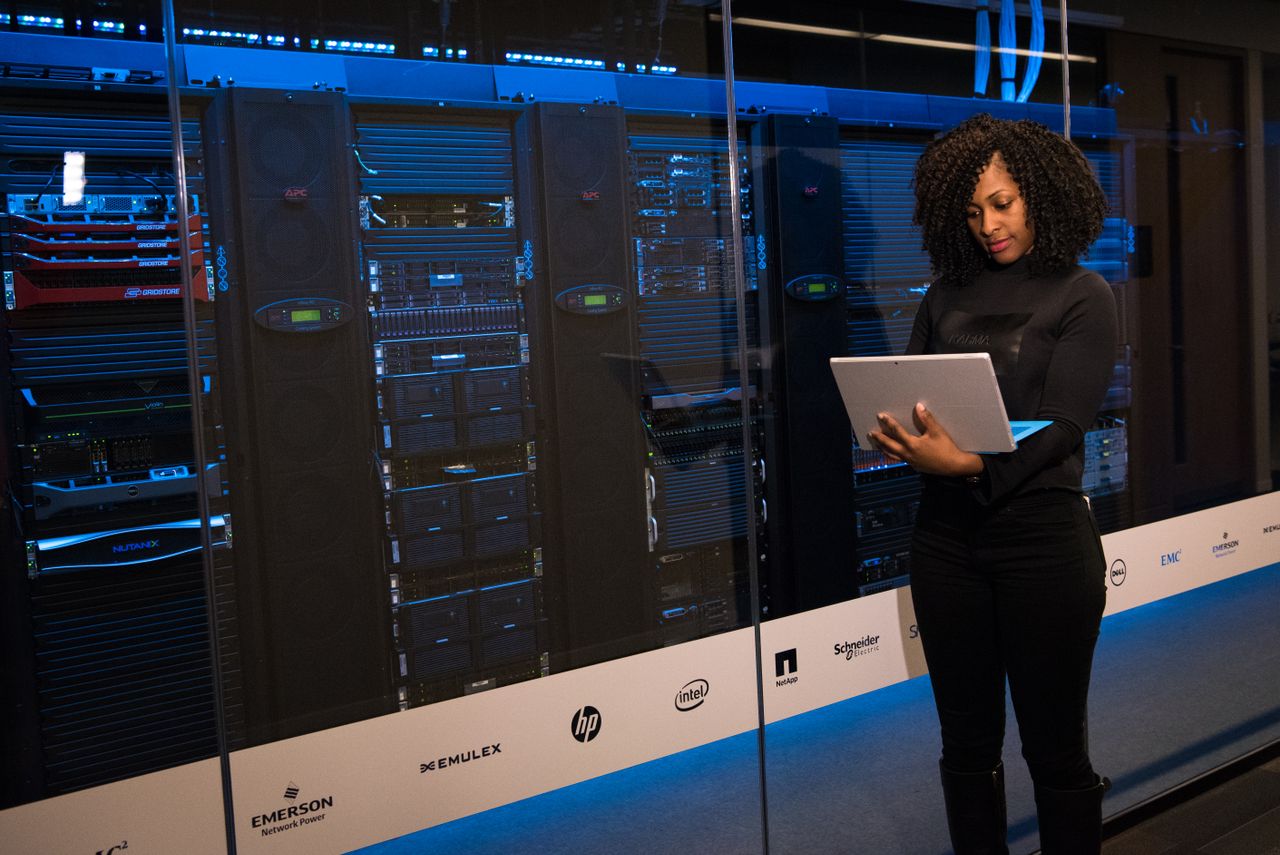 About A female engineer using a laptop while monitoring data servers in a modern server room.